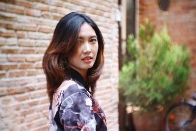 Portrait of young woman standing against brick wall