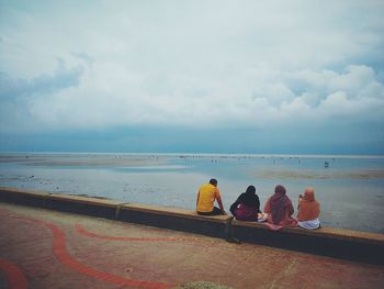 Rear view of family sitting on pier at beach against sky