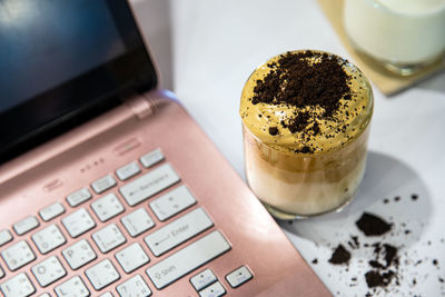 Close up dalgona coffee cup on white desktop next a laptop with blurred cup of milk 