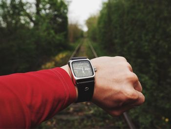 Cropped hand of person wearing wristwatch on railroad track