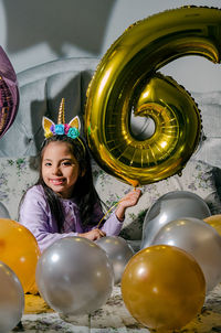 Portrait of cute birthday girl sitting with balloons in bed