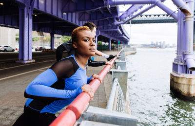 People exercising while standing by railing on bridge over river in city