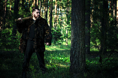 Man with axe standing on field against trees