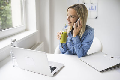 Businesswoman talking on phone while drinking juice at home