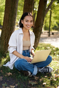 Portrait of young woman using laptop while sitting in forest