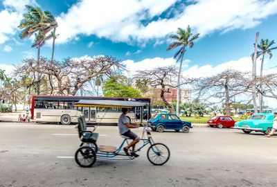 Man riding pedicab on road against sky