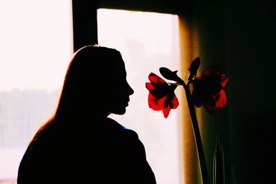 Silhouette woman standing by flower against window at home
