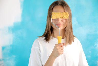 Young woman holding paint roller against blue wall