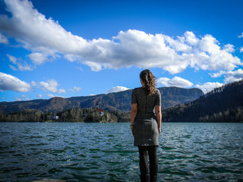 Rear view of woman standing at lakeshore against sky