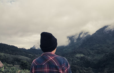 Rear view of man looking at mountains while hiking in forest