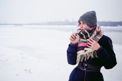 Young woman wearing warm clothing smoking during winter