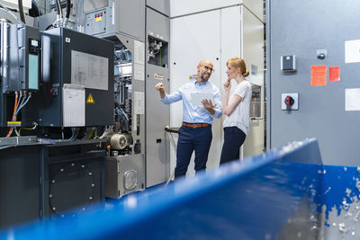 Businessman with tablet showing machine to businesswoman in factory