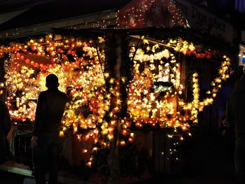 Rear view of man standing at illuminated market stall at night during christmas