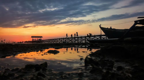 Silhouette bridge over sea against sky during sunset at untia beach, makassar city indonesia.