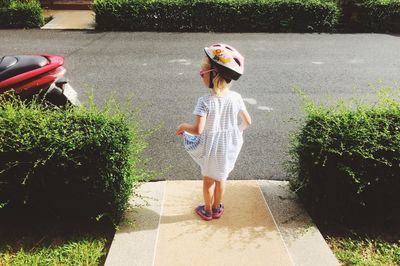 Full length rear view of girl wearing helmet standing on driveway by plants