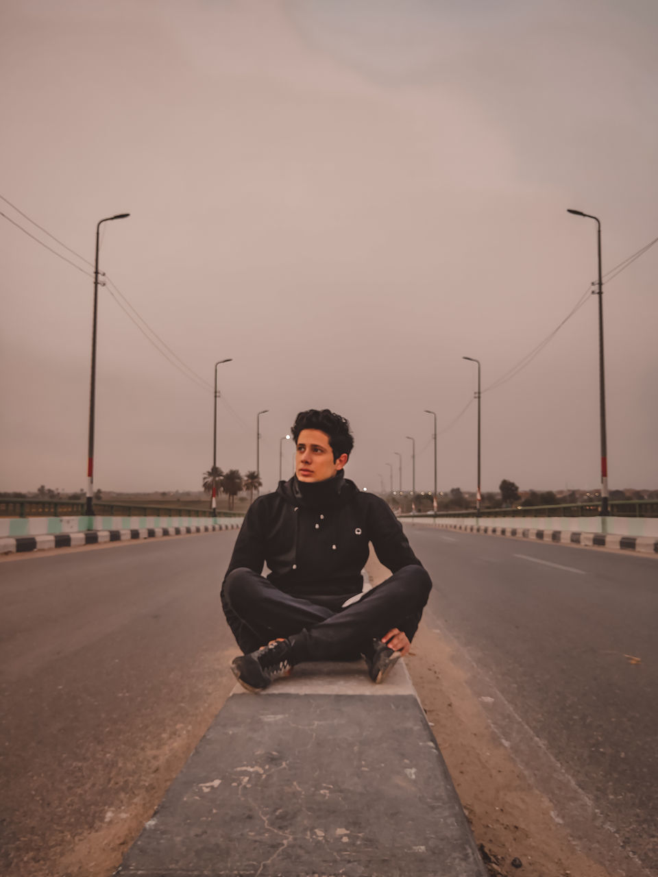 one person, sky, adult, full length, road, transportation, lifestyles, nature, city, men, front view, clothing, copy space, young adult, architecture, street, portrait, looking at camera, sitting, morning, leisure activity, street light, cool attitude, outdoors, technology, sports, serious, casual clothing