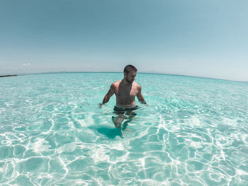 Shirtless man swimming in sea against clear sky
