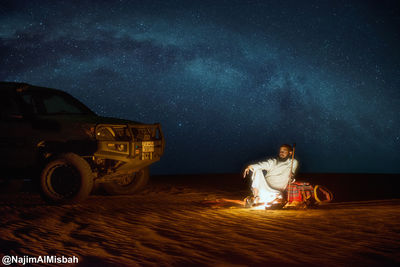 Digital composite image of woman sitting by car at night