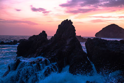 Rock formations in sea against sky during sunset