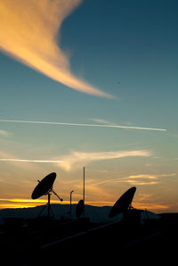 Silhouette of satellite dishes against sky during sunset