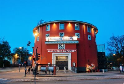 People on illuminated building against clear blue sky