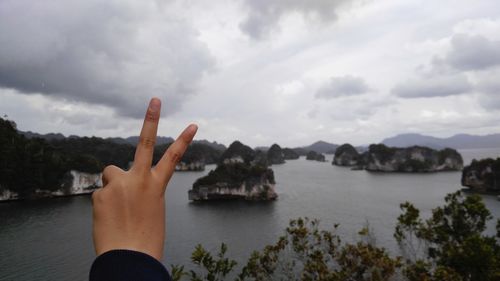 Close-up of hand by lake against sky