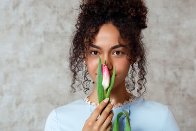 Portrait of smiling young woman holding tulip while standing against wall