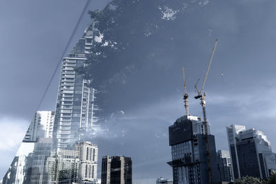 Low angle view of crane and buildings against sky