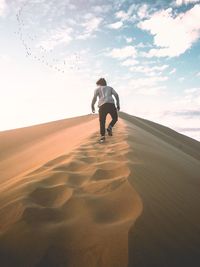 Rear view of man walking on sand against sky