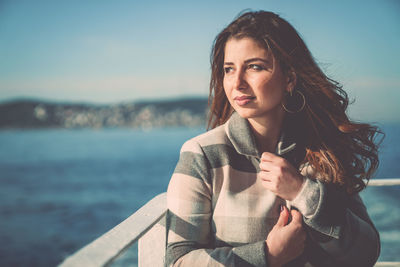 Portrait of young woman standing by sea against sky