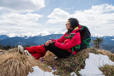 Rear view of man using mobile phone while sitting on rock against sky