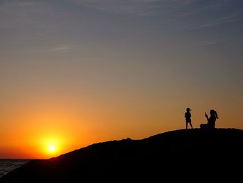 Silhouette people standing on mountain against sky during sunset