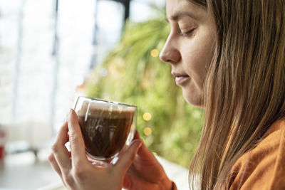 Young pretty caucasian woman holding glass cup of coffee or cocoa and meditating looking at the cup