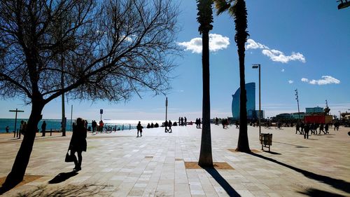 People walking on footpath by street against sky