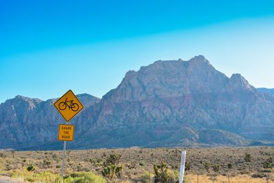 Road sign by mountains against blue sky