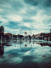 Ferris wheel in city against cloudy sky