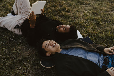 Young man reading diary lying down by male friend on grass in park