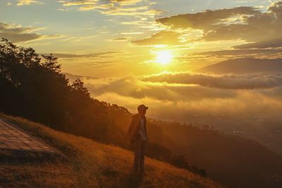 Man standing on mountain peak while looking at sky during sunrise
