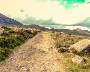 Dirt road amidst landscape against sky