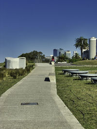 Footpath amidst buildings against clear blue sky