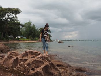 Man standing on rock by sea against sky