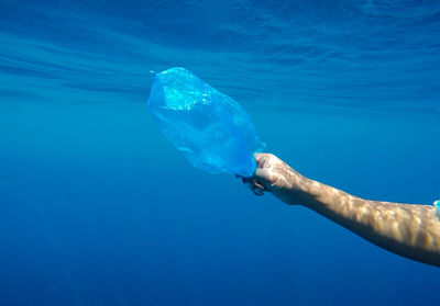 Cropped hand holding plastic bag in sea