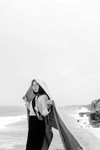 Young woman standing by sea against sky