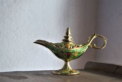 Close-up of ornate oil lamp on table against wall at home