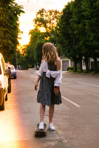 Millennial woman in dress riding a skateboard on street. skater girl on a longboard. cool female 