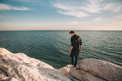 Man standing on rock by sea against sky