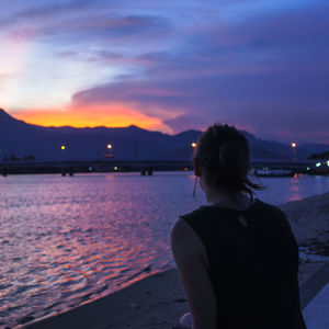 Rear view of woman by river at sunset