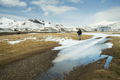 Rear view of man standing on snowcapped mountain against sky