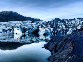 Scenic view of glaciers melting in lake against cloudy sky