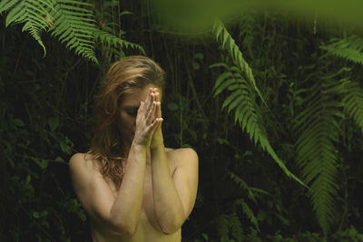 Sensuous woman with hands clasped against plants